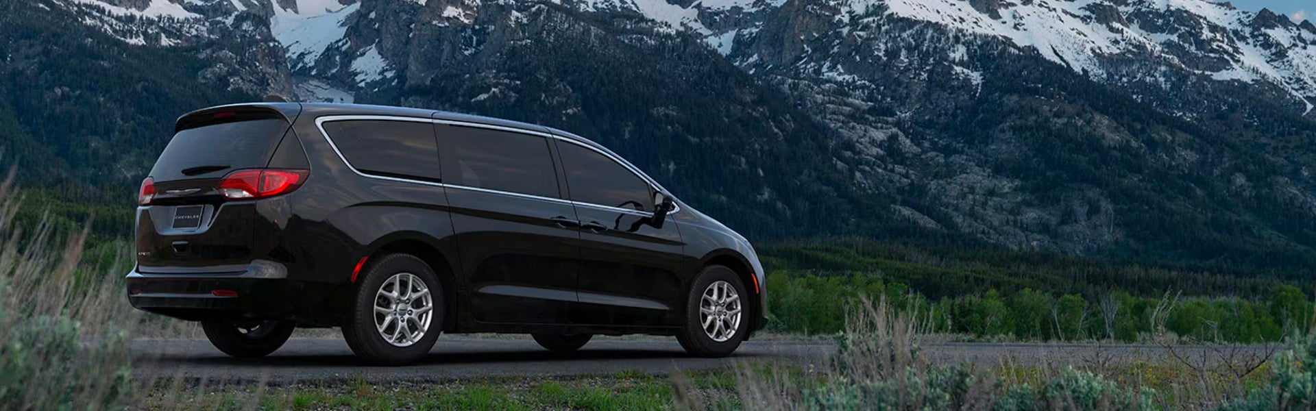 Rear side view of a black 2025 Chrysler Voyager in a mountain setting