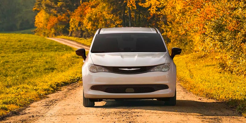 White Chrysler Voyager driving on a forest road in autumn