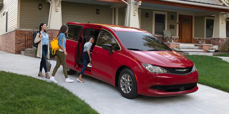 Family loading luggage into a red Chrysler Voyager in a driveway