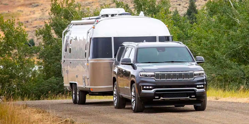 Gray 2025 Jeep Grand Wagoneer running on road towing at back